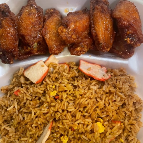 A white takeout container holds golden-brown fried chicken wings and fried rice with crab sticks.