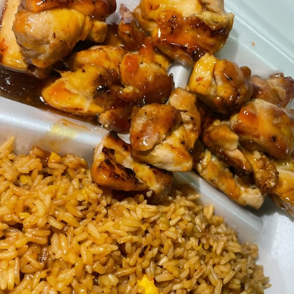 Sweet and sour chicken pieces with fried rice in a white takeout container.