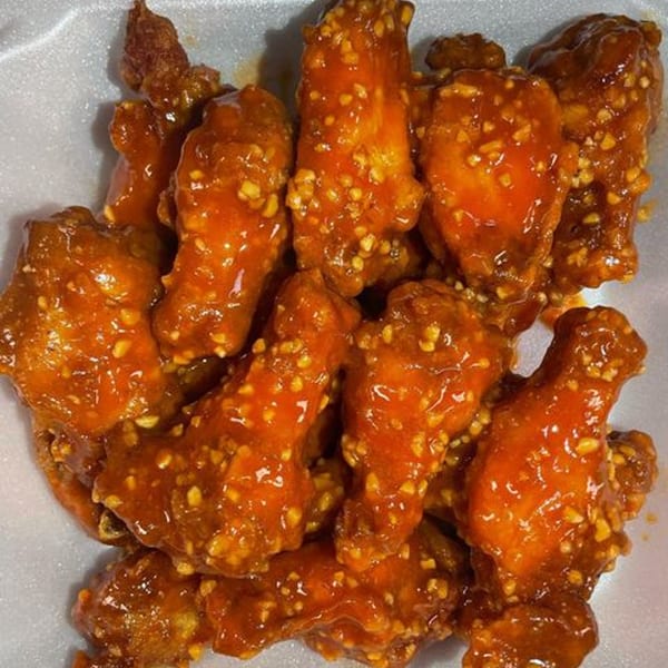 Close-up of several Wings Bomb chicken wings coated in a glossy orange sauce with visible garlic bits.